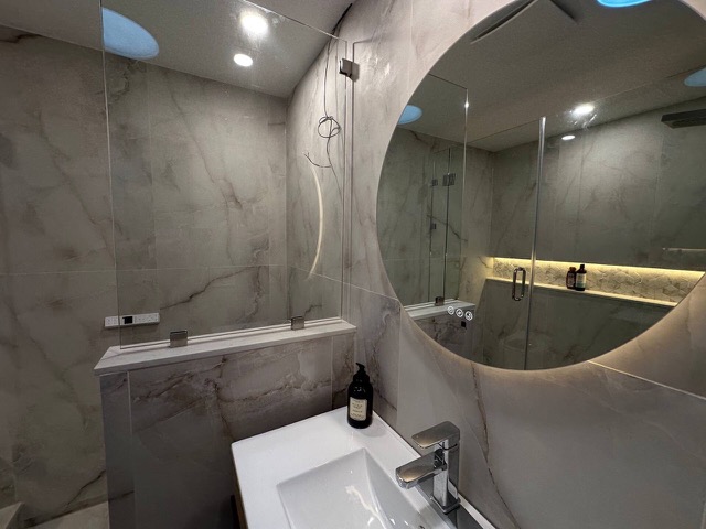 Second bathroom vanity with a backlit round mirror beside the glass shower