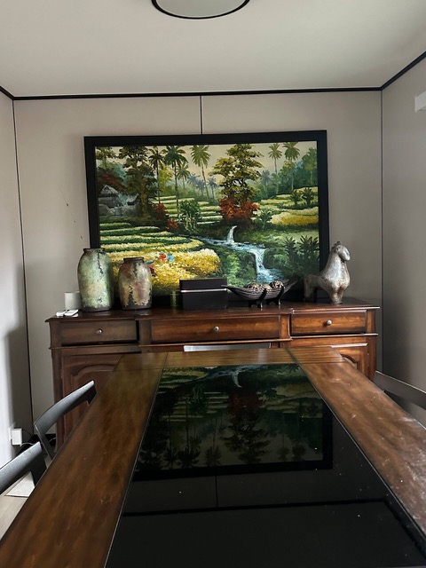 Glass-topped wood dining table in front of the sideboard and a large landscape painting