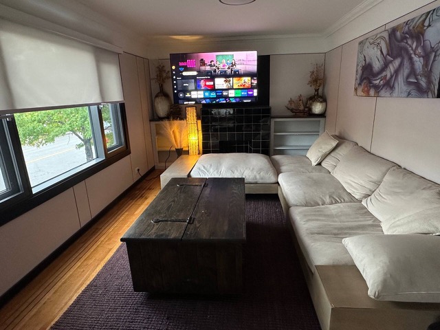 Living room with a white sectional sofa, a wooden chest coffee table and a TV over black tile