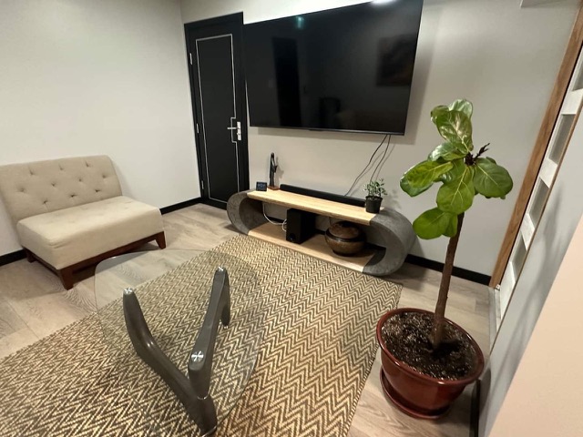 Sitting area with a tufted settee, a glass coffee table, a wall TV on a curved wood console and a fiddle-leaf fig
