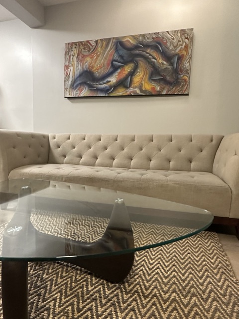 Beige tufted sofa under a large abstract painting, with a glass coffee table